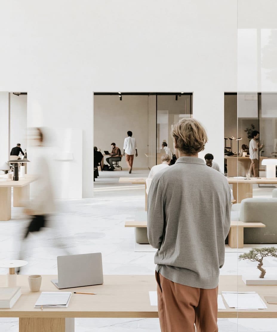 A bright, open-plan modern office where people work at minimal light-wood desks.